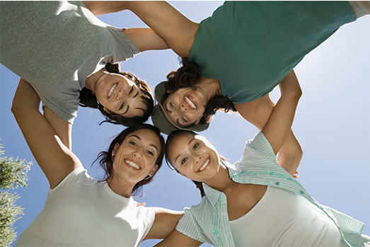 Esta foto se compone por cuatro mujeres jóvenes que se abrazan entre si formando un circulo, la perspectiva de la fotografía es de abajo hacia arriba.